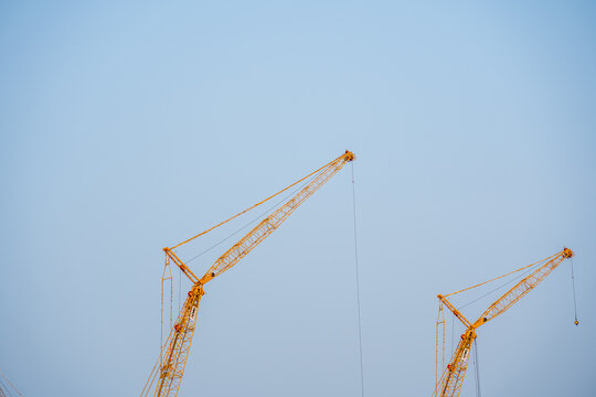 Two Yellow Construction Cranes Against Clear Light Blue Sky