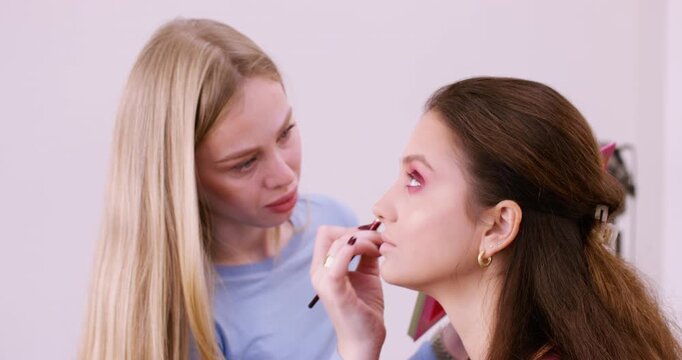 Aesthetic visage. Artistic makeup. Female professional beautician applying eyeshadow to eyelid using brush at workspace indoor.