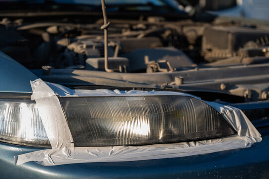 Close-up of a car headlight covered with tape around the perimeter during polishing.