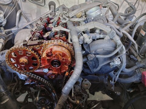 Detailed close-up of a modern internal combustion engine with the valve cover removed, exposing the double overhead camshaft (DOHC) system, timing chain, cam sprockets, tensioners and cam gears