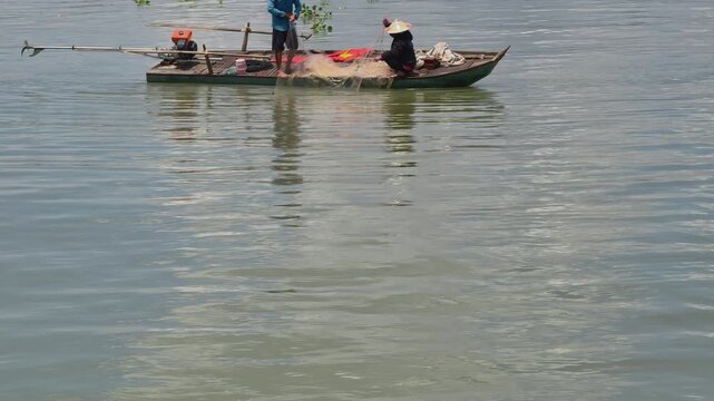 Local fishermen working together, pulling and sorting fishing net on a small wooden boat in the Mekong Delta, Vietnam