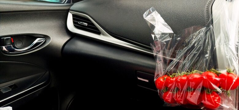 Fresh red cherry tomatoes on the vine in a plastic bag placed on a modern car dashboard during a road trip.