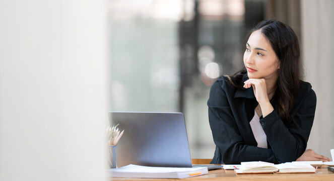 Pensive young Asian businesswoman thinking and looking away at office desk