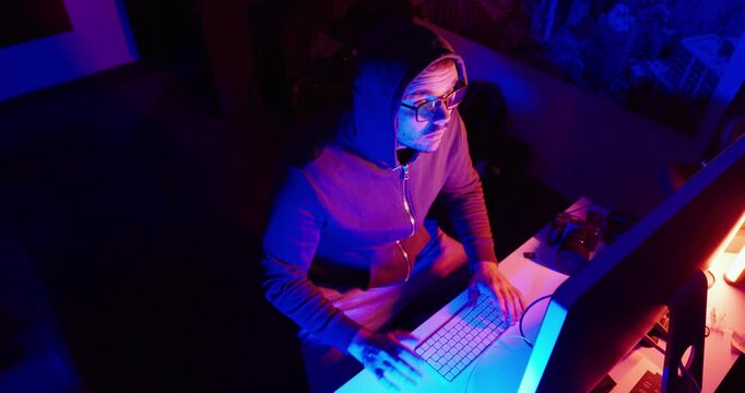 Top-down view of a woman working at a desktop computer in a modern workspace illuminated by colorful blue and pink lighting. Concept of remote work, digital technology, productivity, content creation