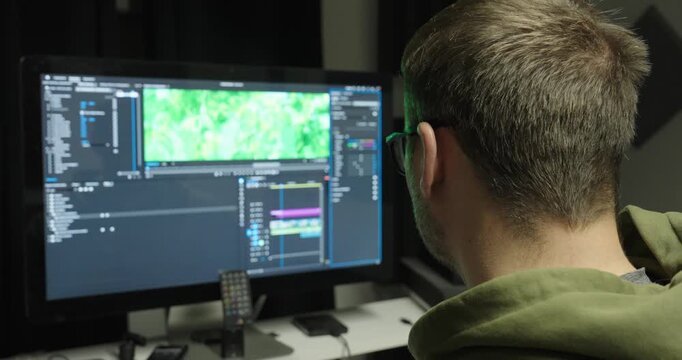Rear view of a video editor working on a computer with Adobe Premiere Pro video editing software. Concept of post-production, content creation, filmmaking, and digital media production.