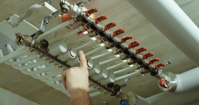 Person checking the valves and flow indicators on an underfloor heating manifold during a system inspection.