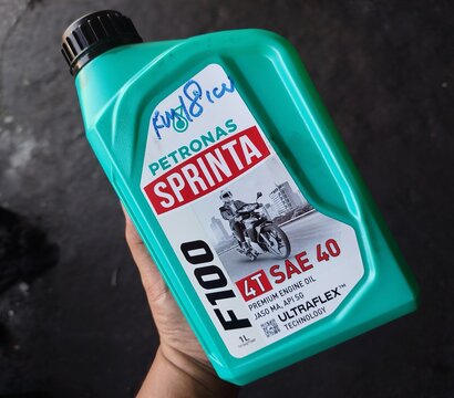 KUALA TERENGGANU MALAYSIA- JUNE 23. 2026. Close-up of a hand holding a 1-liter green plastic bottle of Petronas Sprinta F100 4T SAE 40 premium motorcycle engine oil against a dark textured background