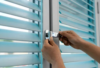 Hands adjusting the heavy silver metal crank of a translucent cyan aluminum louver. © stefanholm