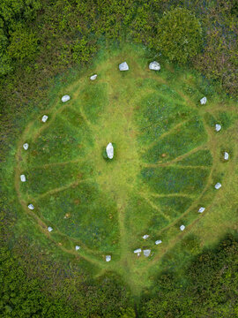 Aerial view of the Boscawen-un Stone Circle featuring its central standing stone and outer ring of stones set in a lush green field in Penzance, England, United Kingdom.