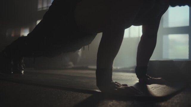 Athletic man performing pushups during intense strength training session in dark atmospheric gym.