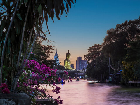 View of big Buddha statue in Bangkok, Thailand (Wat Pak Nam Phasi Charoen) from canal with wooden houses and long tails boats