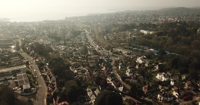 Aerial view of the coastal town of Torquay featuring winding streets, dense residential housing, and lush greenery under soft daylight Torquay, England, United Kingdom.