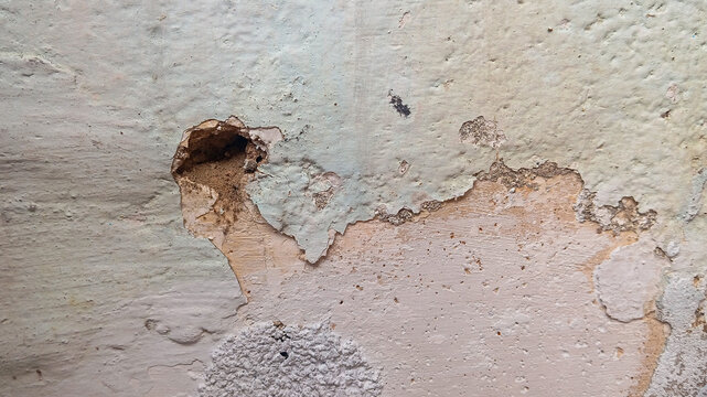 Close-up of a damaged painted wall with peeling paint, cracked plaster, and surface deterioration caused by moisture and aging. 