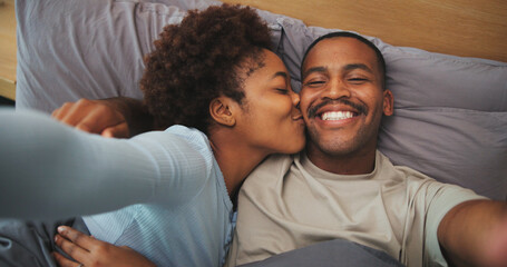 Fototapeta premium Kiss, morning and selfie with black couple in bed at apartment together for bonding, connection or rest. Affection, photograph and security with happy people in bedroom of home for holiday memories