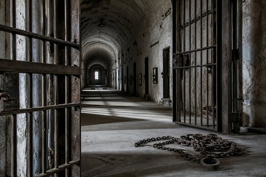 An empty prison corridor with open iron doors and chains on the floor.