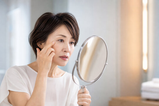 鏡を見て目元のシワや肌を気にする日本人女性