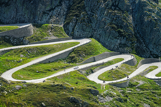 Aerial view of the winding road of Passo del San Gottardo with stone retaining walls and green alpine slopes in Airolo, Ticino, Switzerland.