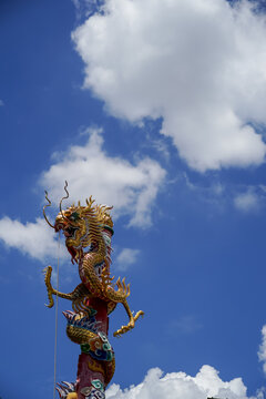 Ornate golden dragon statue coiled around a pillar against a bright blue sky