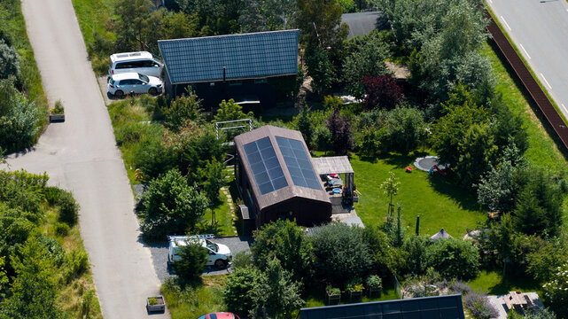 Aerial view of a modern house with solar panels on the roof, surrounded by a lush garden, trees, and a quiet residential street in Almere, Flevoland, Netherlands.