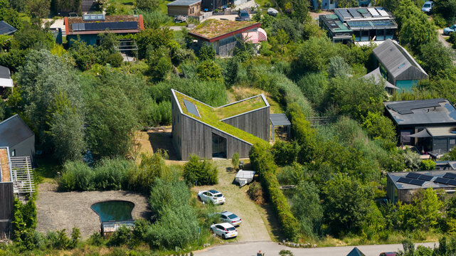 Aerial view of a modern house with a green roof nestled in a lush, wooded residential area with solar panels, private driveway, and surrounding greenery in Almere, Flevoland, Netherlands.