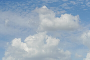 Fluffy white cumulus clouds drift across a bright blue sky on a sunny day © Thanakrit