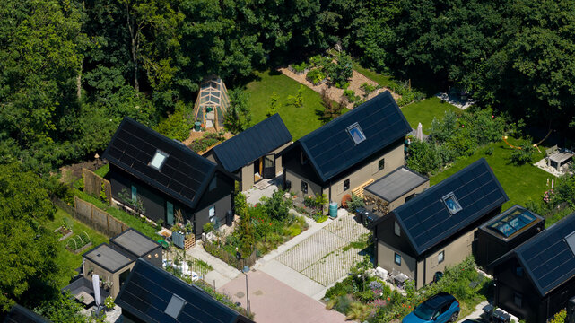 Aerial view of modern small houses with solar panels, lush green gardens, and paved pathways in a residential area in Almere, Flevoland, Netherlands.