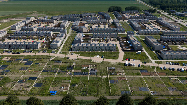 Aerial view of a modern residential neighborhood with rows of houses, parking areas, and adjacent community garden plots in Almere, Flevoland, Netherlands.