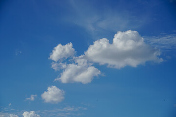 Fluffy white cumulus clouds drift across a vibrant blue sky on a clear day © Thanakrit