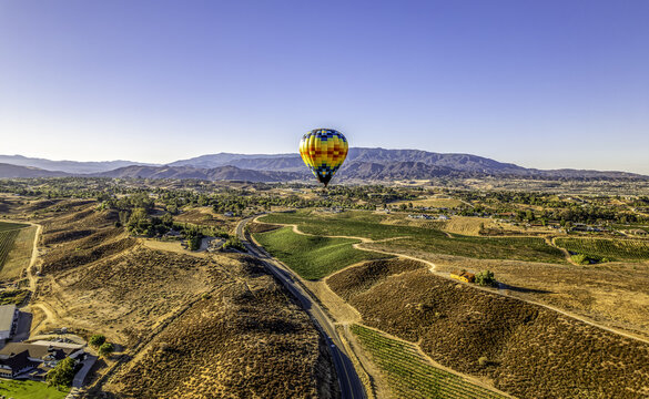 Aerial view of a colorful hot air balloon floating over the rolling hills and vineyards of Temecula, California, United States.