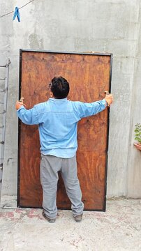 Young Man Adjusting Wooden Door Against Concrete Wall