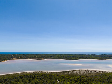 Aerial view of Lake Preston with calm waters, surrounded by coastal vegetation and sand dunes, with the Indian Ocean in the background in Preston Beach, Western Australia, Australia.