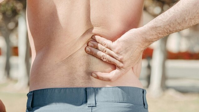 Man holding painful lower back outdoors evoking spine injury vertebrae strain osteochondrosis and medical orthopedic treatment web banner advertising concepts.