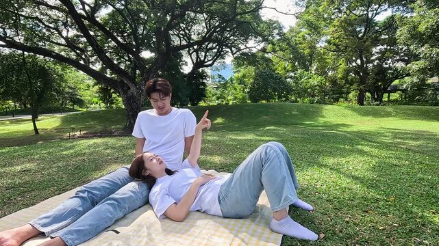 Young Asian Couple Relaxing on Picnic Blanket Under Large Tree