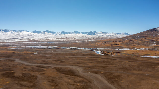 Aerial view of the vast brown plains, winding river, and snow-capped mountain peaks of Deosai National Park, Astore, Gilgit, Pakistan.