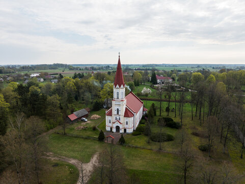 Aerial view of Rucava evangelical lutheran church with its red spire, surrounded by lush green trees and rural landscape in Rucavas pagasts, Dienvidkurzemes novad, Latvia.