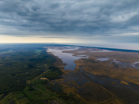 Aerial view of Lake Pape surrounded by wetlands, forests, and fields under a dramatic cloudy sky in Rucava parish, South Kurzeme Municip, Latvia.