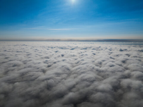 Aerial view of a vast layer of white clouds stretching to the horizon under a clear blue sky in Latvia.