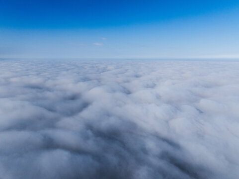 Aerial view of a vast expanse of dense white clouds stretching to the horizon under a clear blue sky in Latvia.