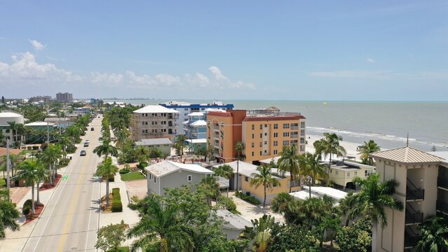 Aerial view of the coastal town of Fort Myers, featuring palm trees, multi-story buildings, a road parallel to the beach, and the Gulf of Mexico in Fort Myers, Florida, United States.