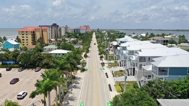 Aerial view of a coastal road lined with palm trees, residential houses, and a parking lot near the beach in Fort Myers, Florida, United States.