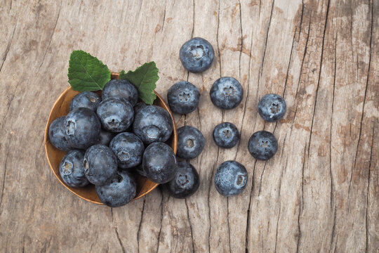 Top view of fresh blueberries in a wooden bowl with mint leaves on rustic wooden background.