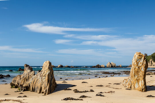 Large metamorphosed rocks shaped and folded by volcanic activity and then weathered and eroded by the elements, stand on the beach at Glasshouse Rocks at Narooma in New South Wales, Australia.