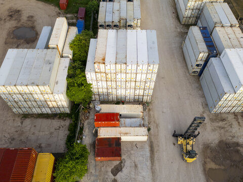 Aerial view of stacked shipping containers in a storage yard with a reach stacker vehicle operating near the containers in Progreso, Yucatan, Mexico.