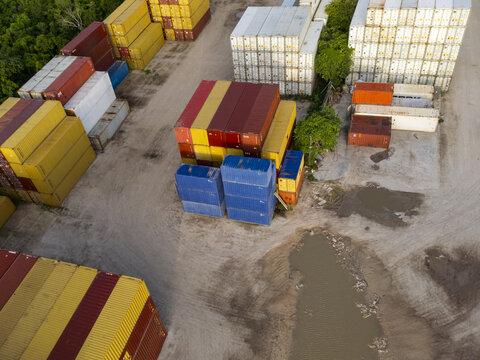 Aerial view of shipping containers stacked in the port of Puerto Progreso, featuring rows of colorful metal containers on a dirt ground with puddles in Progreso, Yucatan, Mexico.