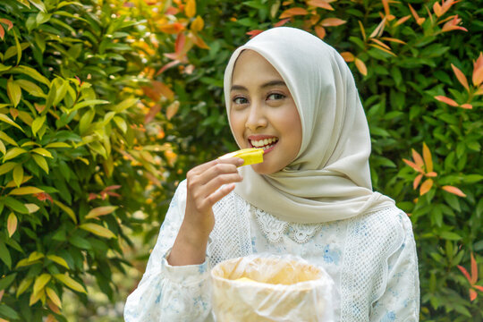 A young Asian Muslim woman enjoys tahu takwa (yellow tofu) in the garden. A typical dish from Kediri, Indonesia.