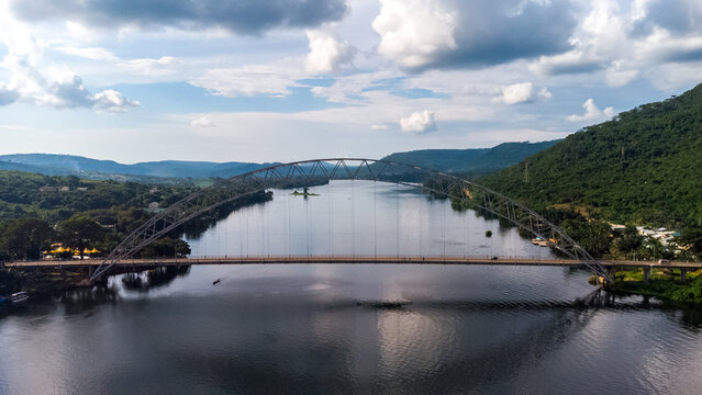 Aerial view of the iconic Adomi Bridge spanning the Volta River, surrounded by lush green hills and a cloudy sky in Atimpoku, Volta Region, Ghana.