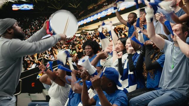 Passionate football capo beating drum and directing blue supporter group from stadium stands during coordinated chant at live soccer match, hardcore fans wave scarves, stadium chants.