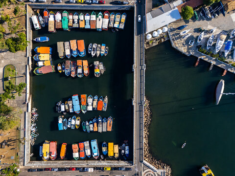 Aerial view of Quadrado da Urca marina featuring colorful fishing boats docked in rows along concrete piers with a road alongside in Rio de Janeiro, Rio de Janeiro, Brazil.