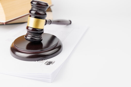 Side angle view of a mahogany judge gavel resting under official legal case documents and verdict papers on a white background panel