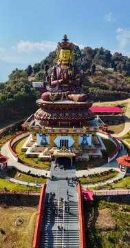 Aerial view of the Chenrezig statue featuring a large colorful Buddha figure on a pedestal, surrounded by a circular courtyard and lush green hills in Darap, Sikkim, India.